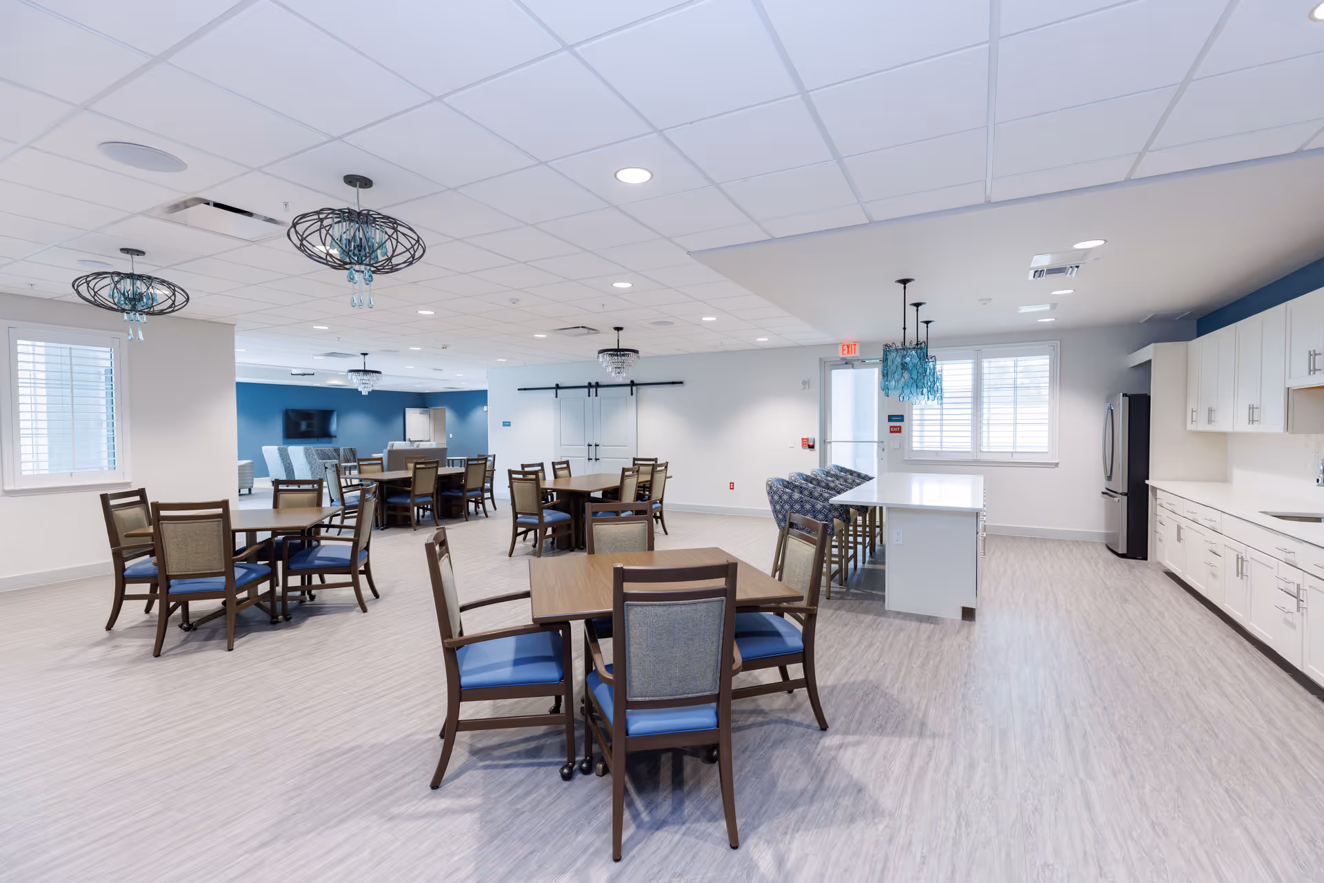 Spacious open communal dining and kitchenette area with multiple tables, chairs, and decorative pendant lights.