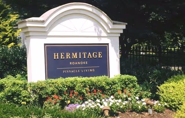 Entrance sign reading 'Hermitage Roanoke Pinnacle Living' set in a landscaped bed of flowers and shrubs.