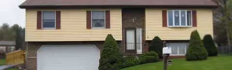 Front view of a beige two-story building with brown shutters, a garage, and a green lawn.
