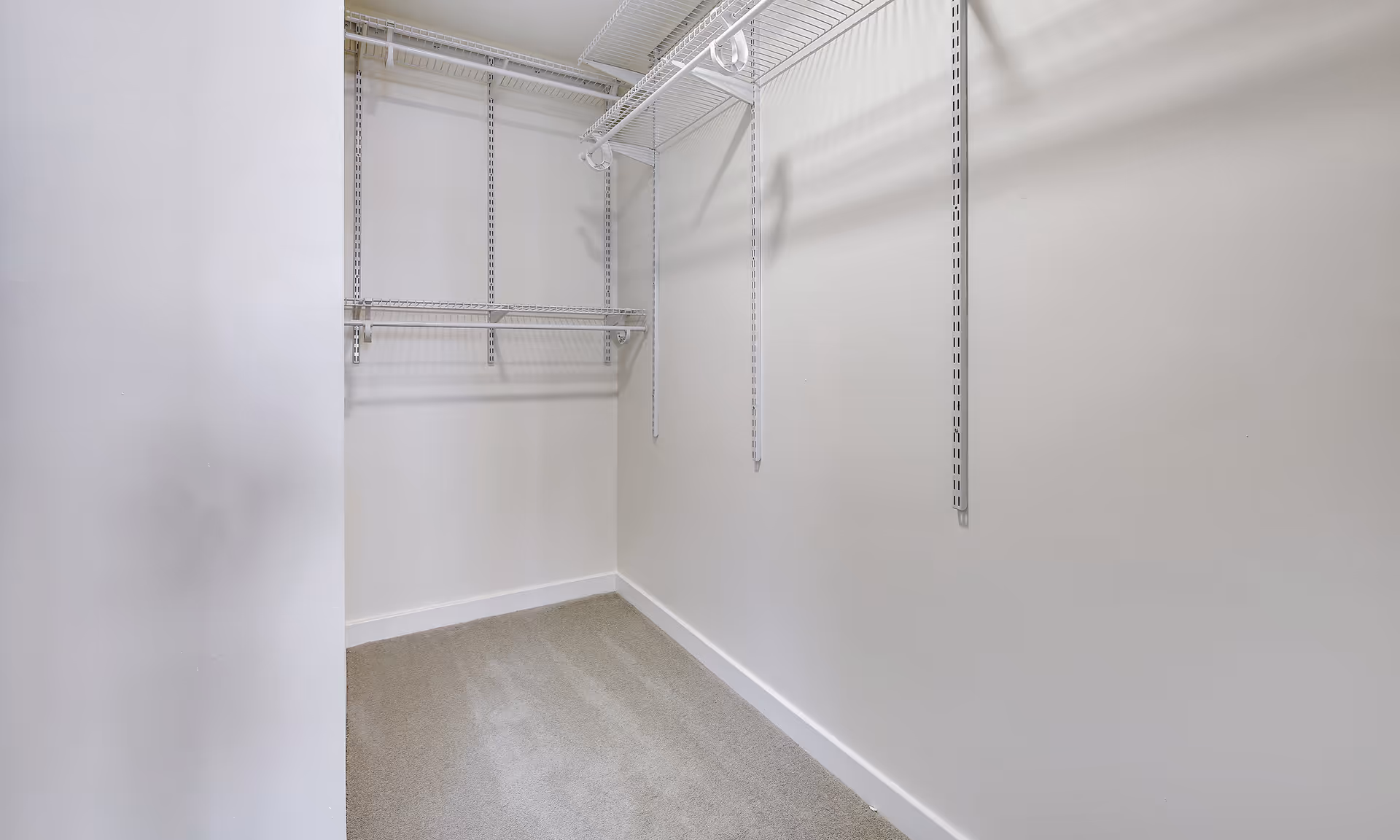 Empty walk-in closet with white wire shelving and light carpeting.