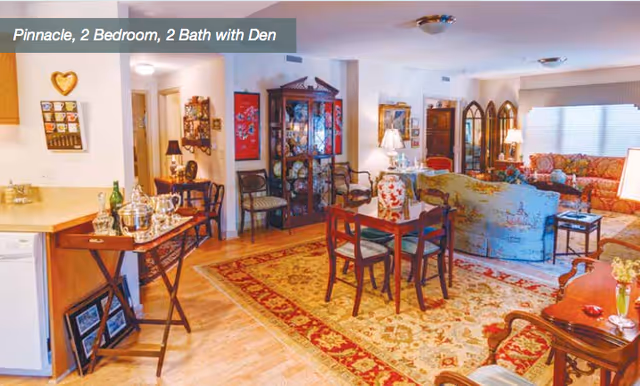 Open-plan living and dining area with hardwood floors, a patterned area rug, several seating pieces, a dining table, and a china cabinet.