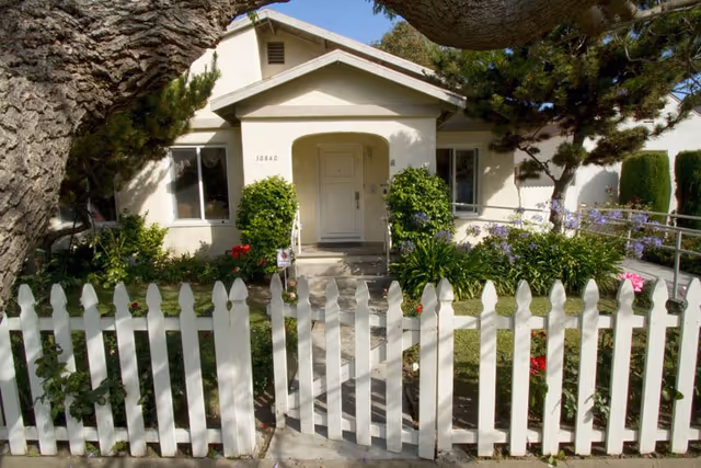Front view of a single-story care home with a white picket fence and garden.