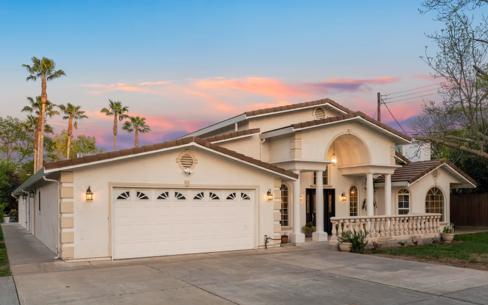 Front exterior of a two-story Mediterranean-style house with a large garage, columns, and a driveway at sunset.