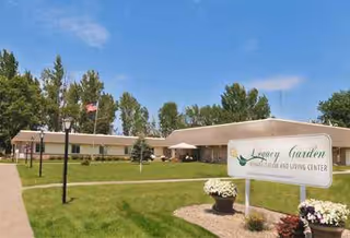 Exterior view of a single-story senior living facility with a green lawn, sign, and flag.