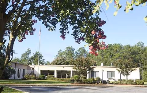Single-story senior living facility with a white exterior, entrance, and manicured landscaping.