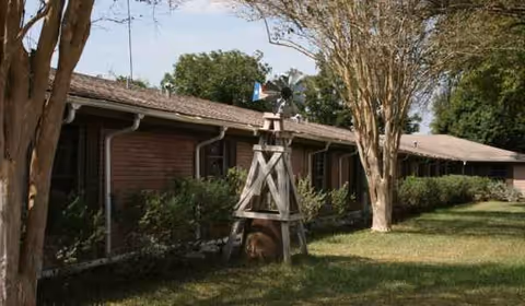 Exterior view of a single-story brick senior facility with trees and a windmill.