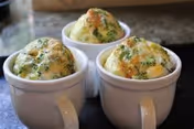 Three white ceramic mugs filled with a baked dish topped with melted cheese and herbs, placed on a dark countertop.
