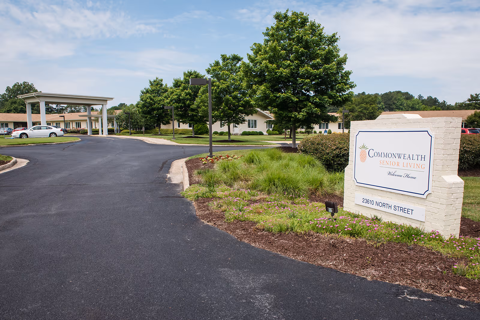 Driveway entrance with landscaping and a sign reading Commonwealth Senior Living in front of the facility buildings.