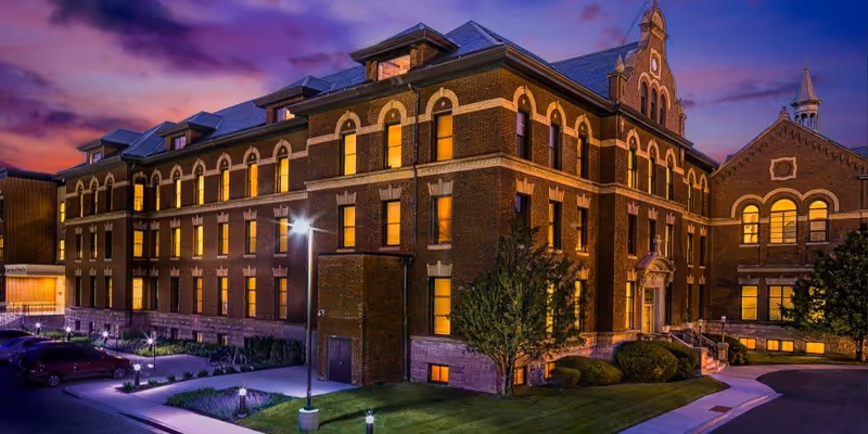 Brick senior living facility exterior at dusk with illuminated arched windows and manicured landscaping