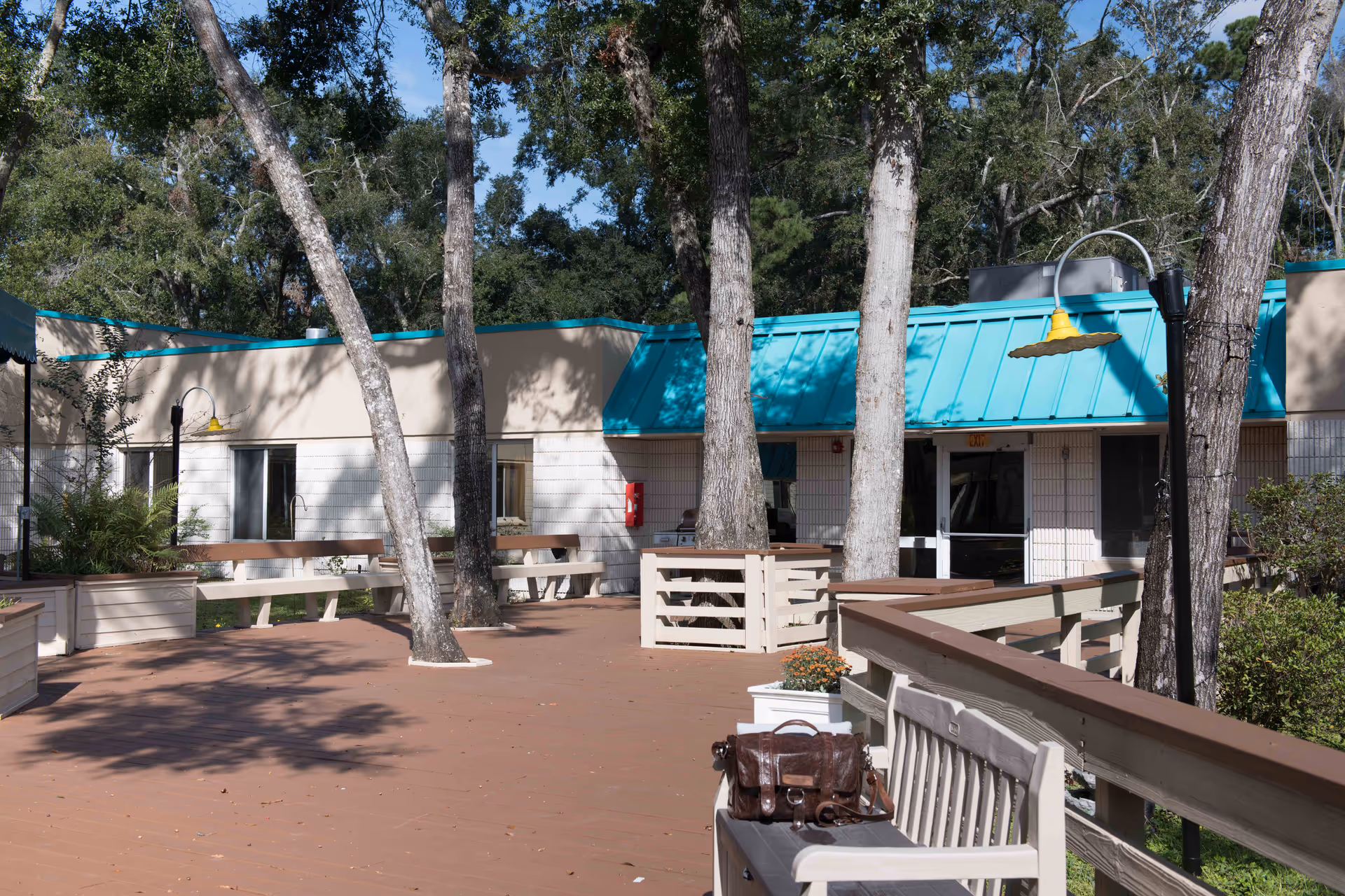Outdoor wooden deck courtyard with benches, trees, and a teal-roofed building facade.