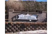 A brick sign for Princeton Health Care Center mounted on a low brick wall with landscaping around it, including bushes and a stone retaining wall in front.