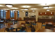 Dining room with several tables and chairs, overhead lights, a serving counter and large windows.