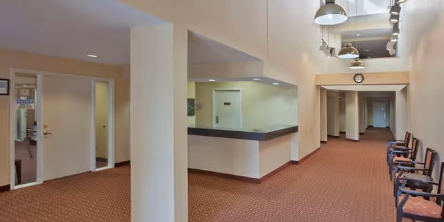 Spacious reception lobby with a check-in counter, columns, and chairs along a carpeted hallway.
