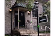 Exterior view of a stone building entrance with steps, railing, and a sign.