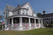 Two-story white building with wraparound porch and patriotic bunting.