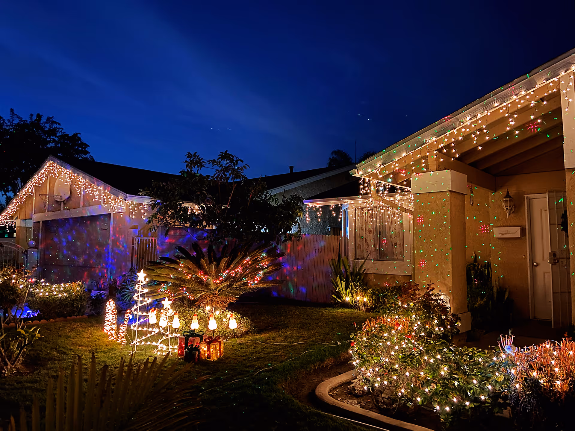 Night exterior of a house with festive Christmas lights and yard decorations