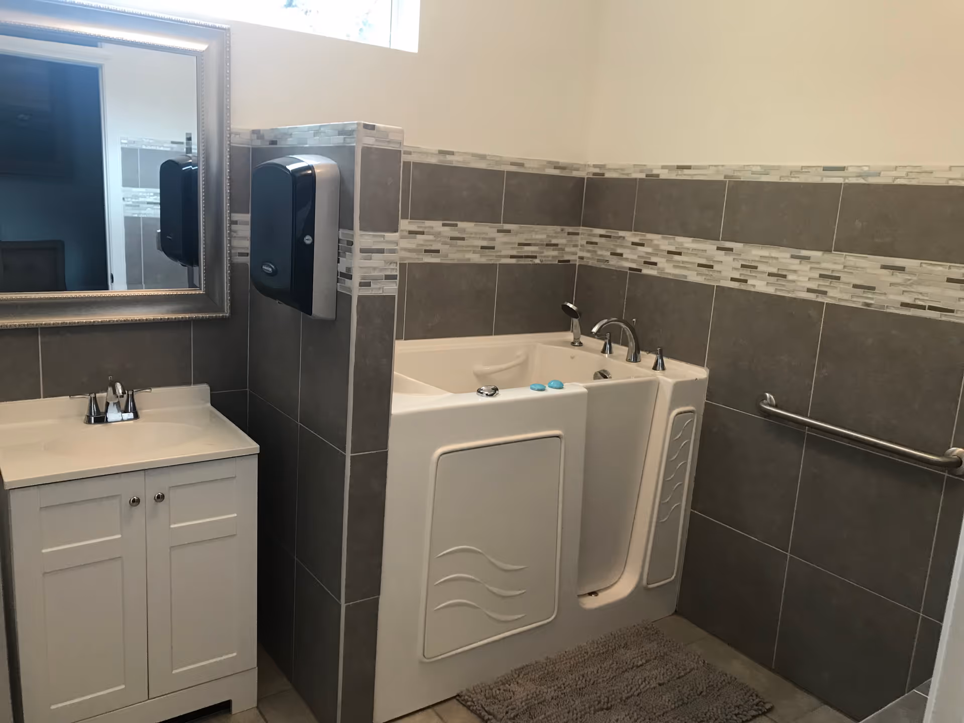 Accessible bathroom featuring a walk-in tub with a door, sink vanity, decorative tile and a grab bar.