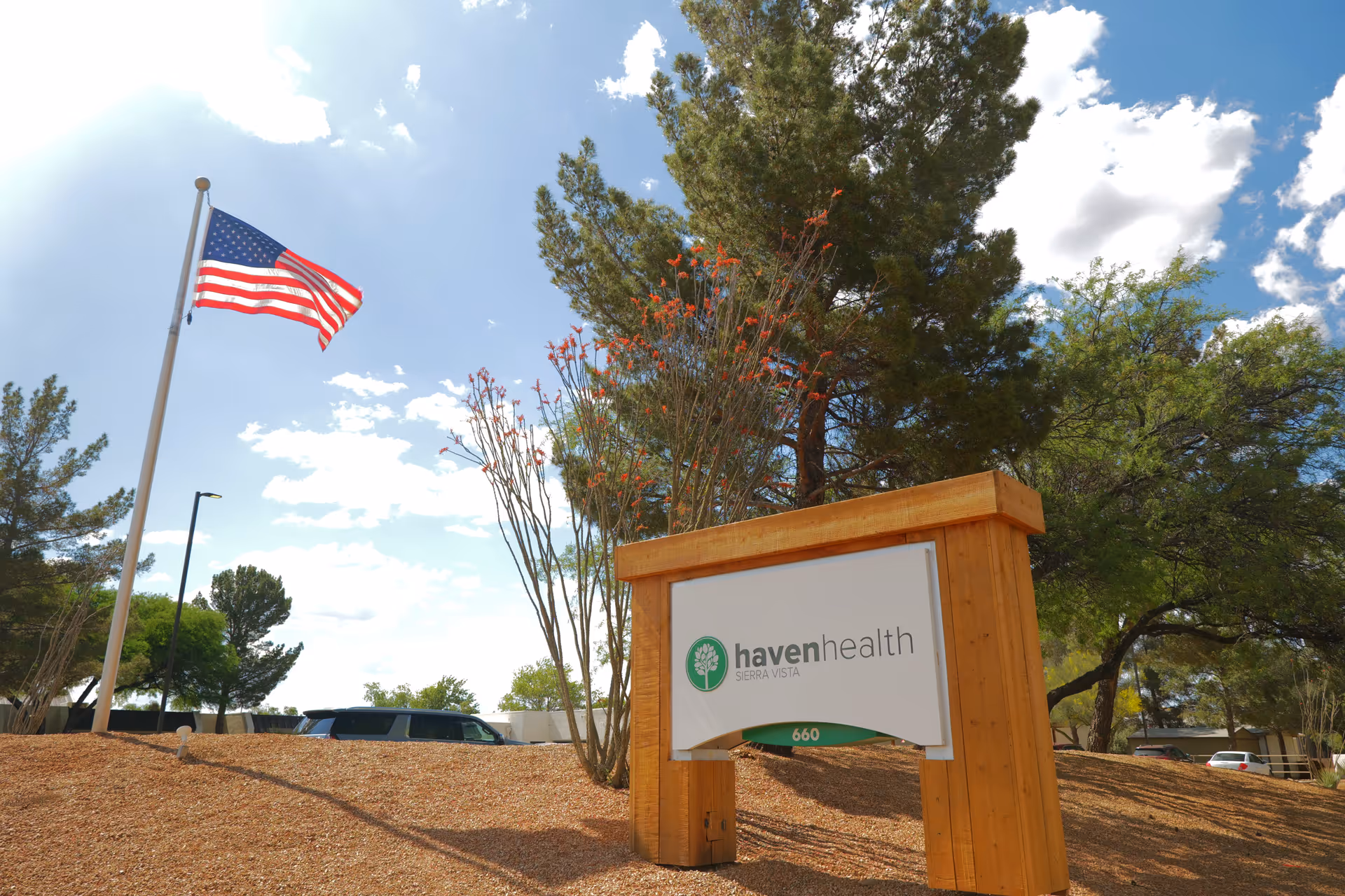Wooden entrance sign for Haven Health Sierra Vista on a landscaped hill with an American flag and trees under a blue sky.