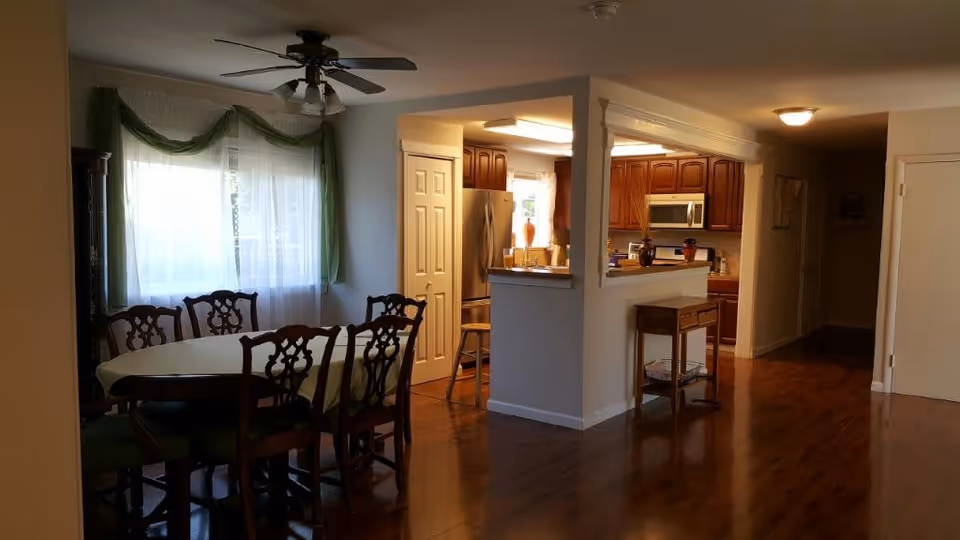 Dining room with a round table and chairs next to an open kitchen with wooden cabinets and hardwood floors.