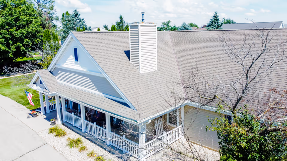 Front exterior of a single-story senior living building with a covered porch, American flag, and a large pitched roof.