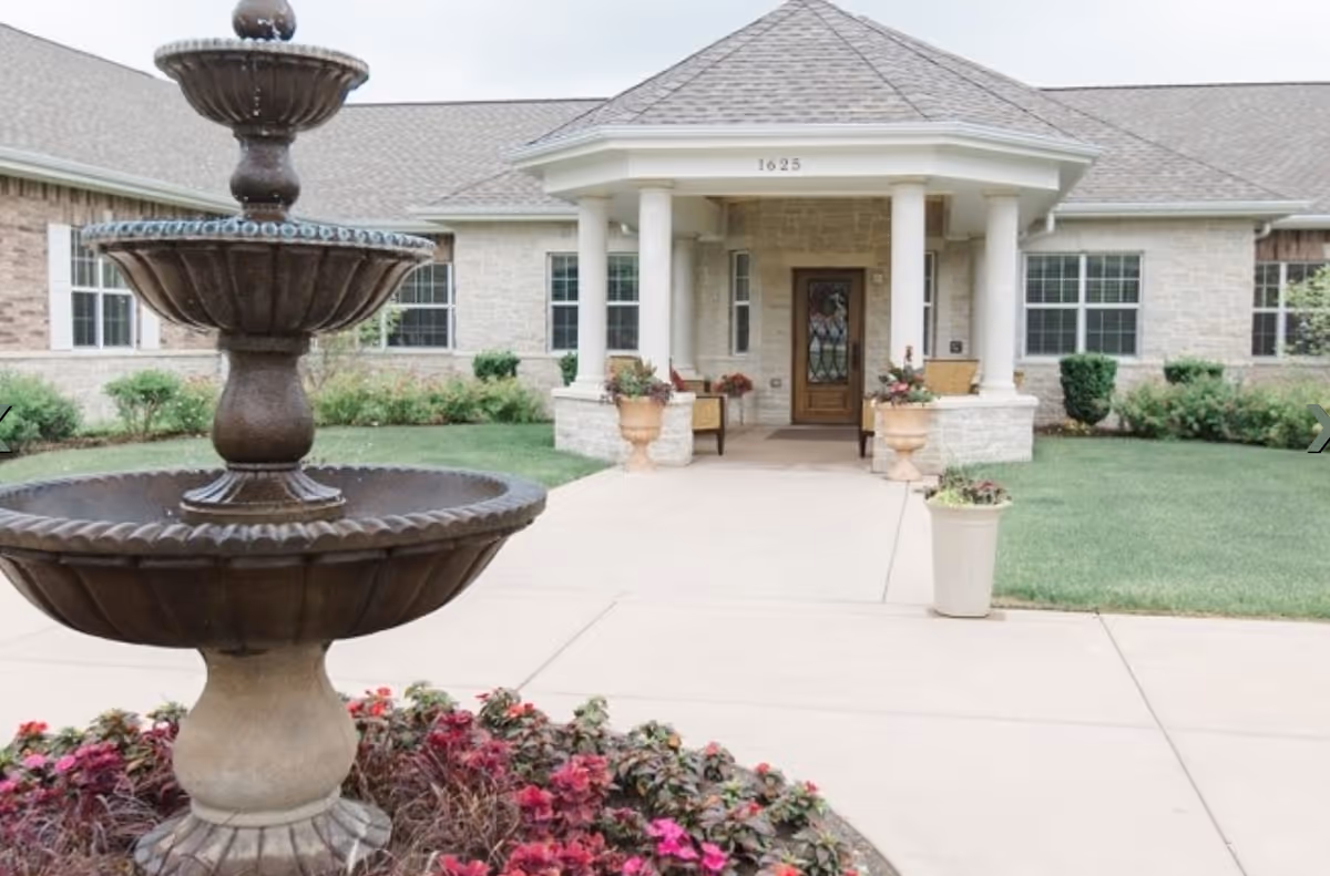 Stone entrance with pillars, fountain in foreground, and lawn at Volante Senior Living of Arlington Heights.