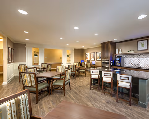 Spacious senior dining and lounge area with multiple tables, upholstered chairs, and a small bar/kitchenette.