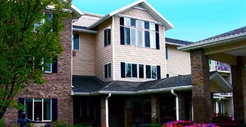 Two-story beige senior living building with large windows and brick columns at the entrance.