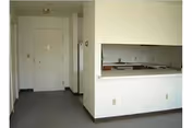 Small apartment interior with an entry door, carpeted living area and a kitchen pass-through countertop.