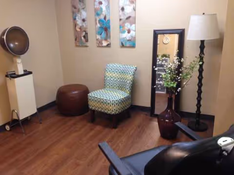 Hair salon area in a senior facility with patterned chair, mirror, lamp, and vase.