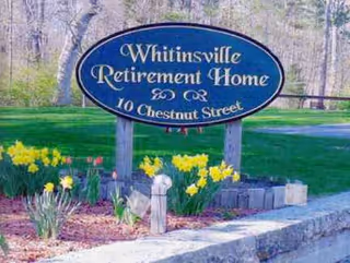 Blue oval sign reads Whitinsville Retirement Home at 10 Chestnut Street, with flowers and green lawn.