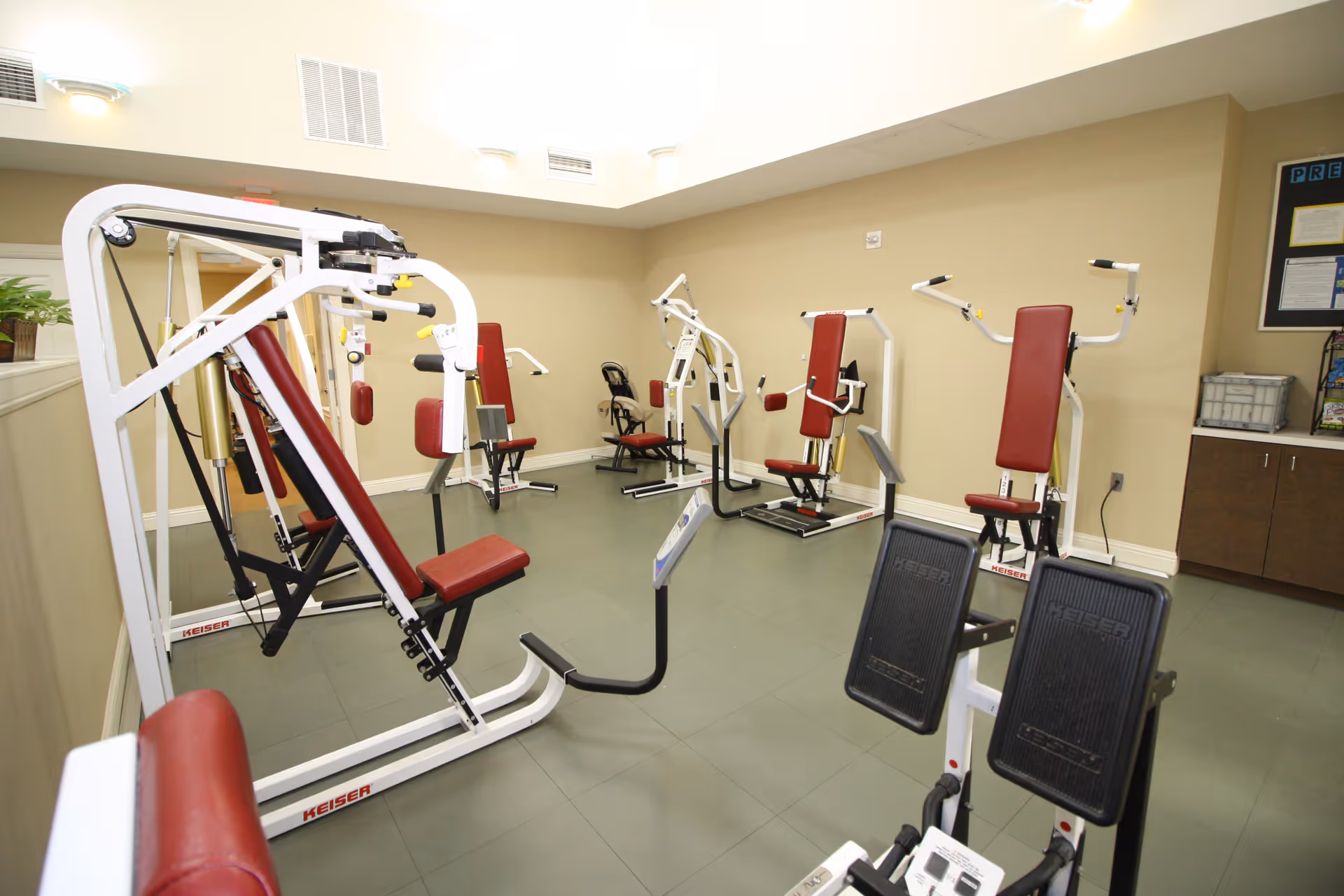 Fitness room with several red-padded strength-training machines arranged on a tiled floor.