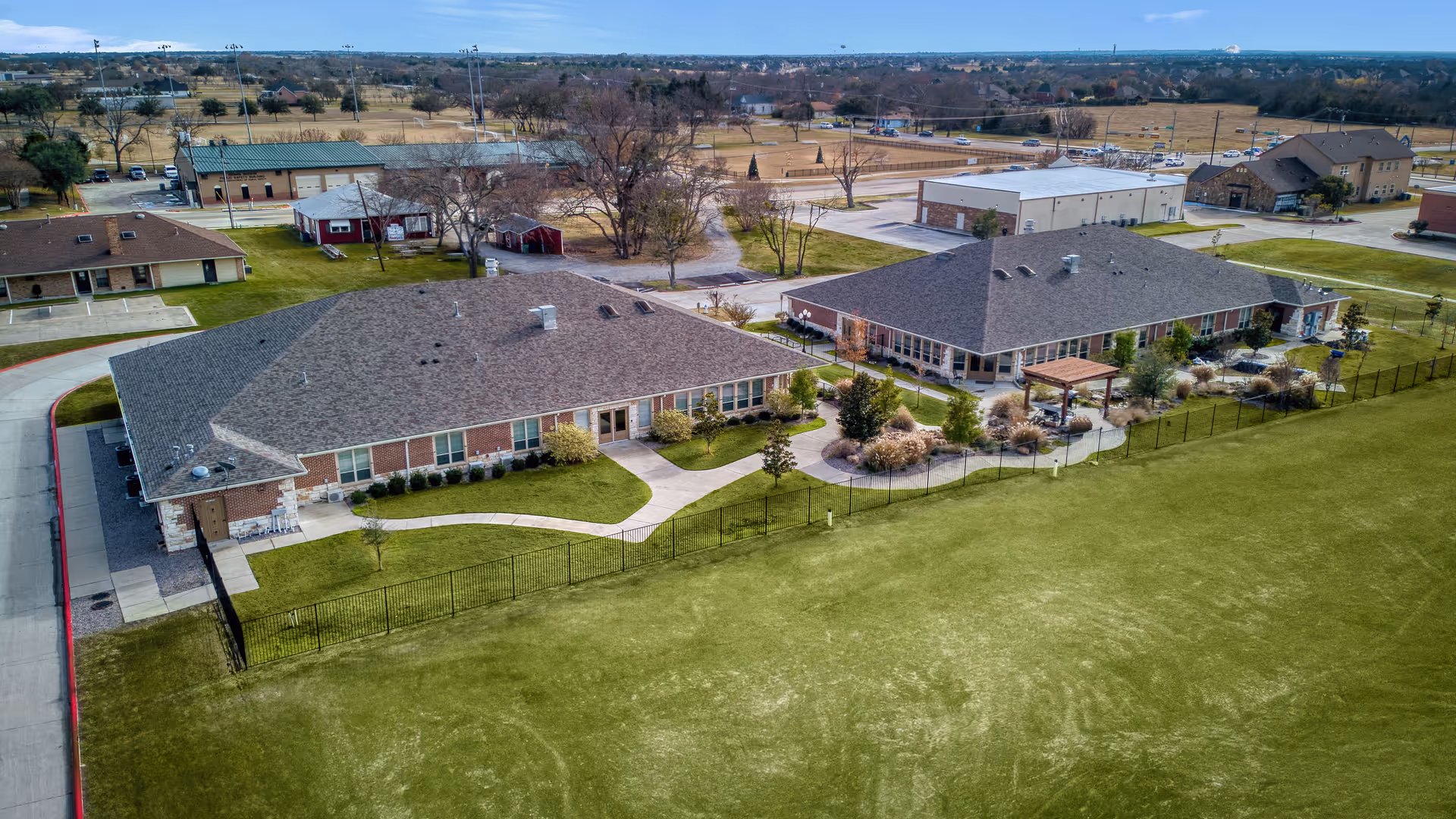 Aerial view of two single-story assisted living buildings with a landscaped courtyard and fenced lawn.