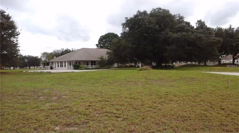 Single-story building set behind a large grassy lawn with a big oak tree under a cloudy sky.