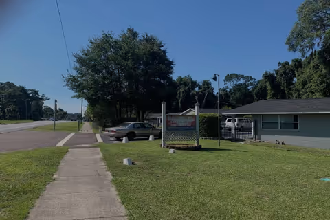 Exterior view of Mayflower Assisted Living showing a tree-lined street, sidewalk, sign, and building.
