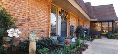 Brick exterior of a senior living facility with front entrance, walkway, and lush landscaping.