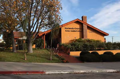 Front exterior of Hacienda Grande Senior Assisted Living with trees and shrubs.