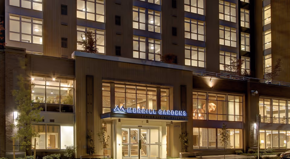 Night view of the illuminated entrance and facade of the Merrill Gardens at Ballard senior living building.