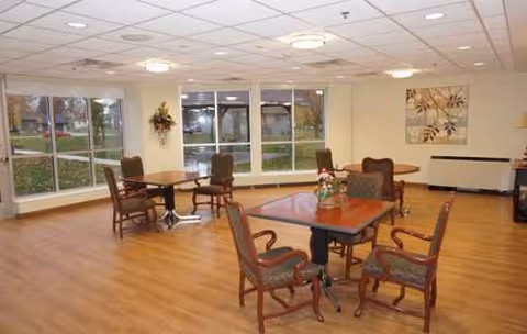 Bright dining area with wooden tables, chairs, and large windows in a senior living center.