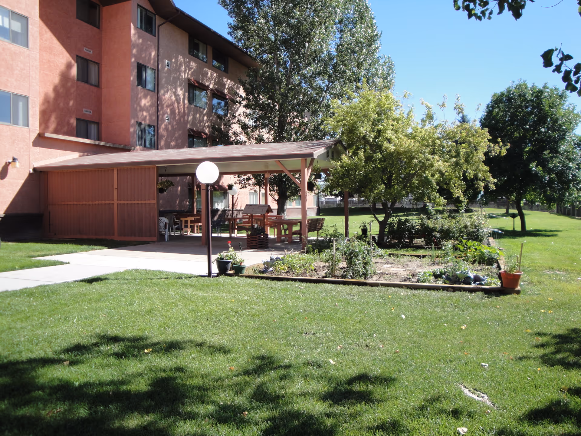 A view of the outdoor area of Anciano Towers featuring a garden, seating area, and lush green grass.