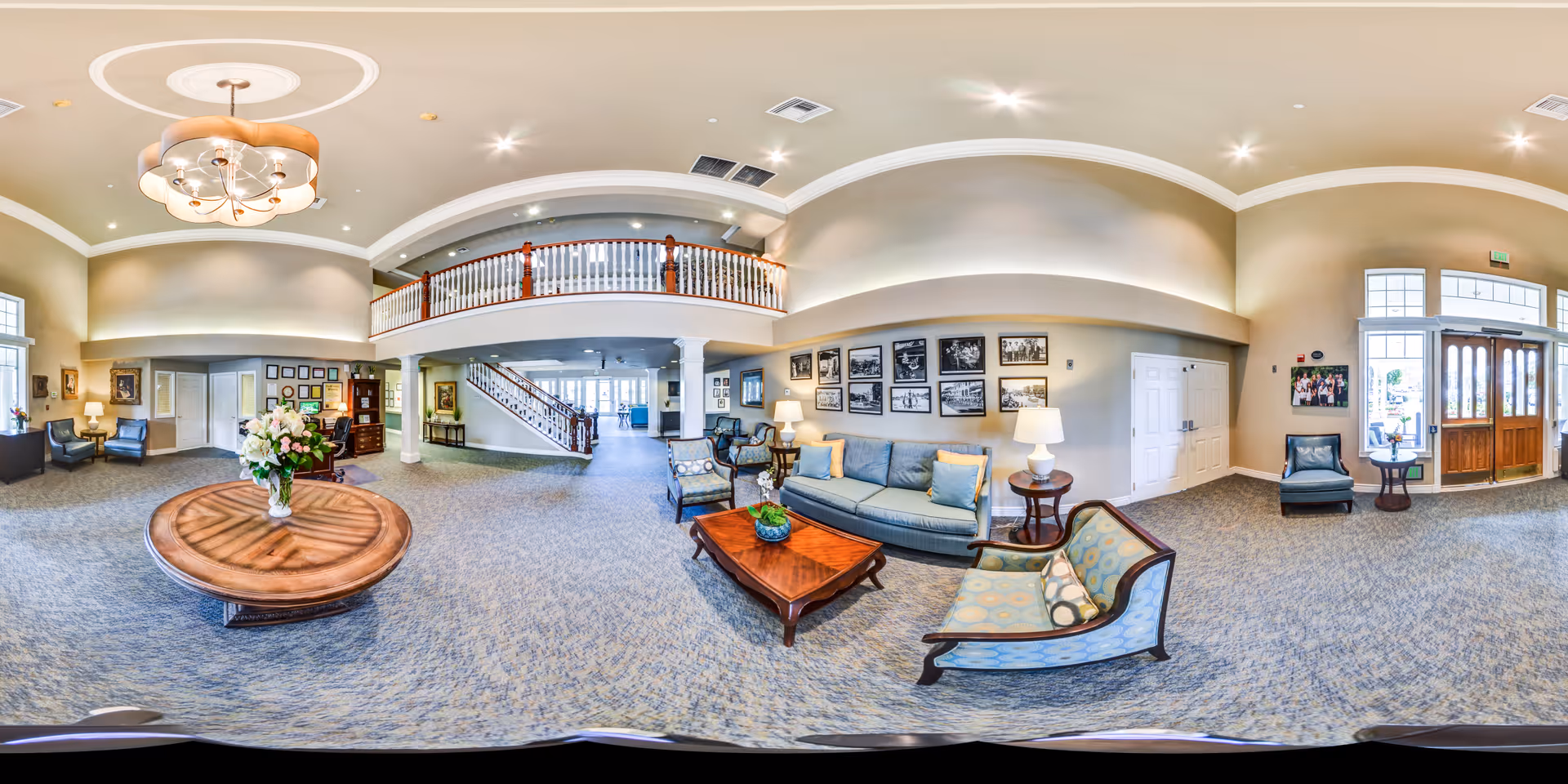Spacious two-story lobby with seating areas, a central round table with flowers, staircase and upper balcony.