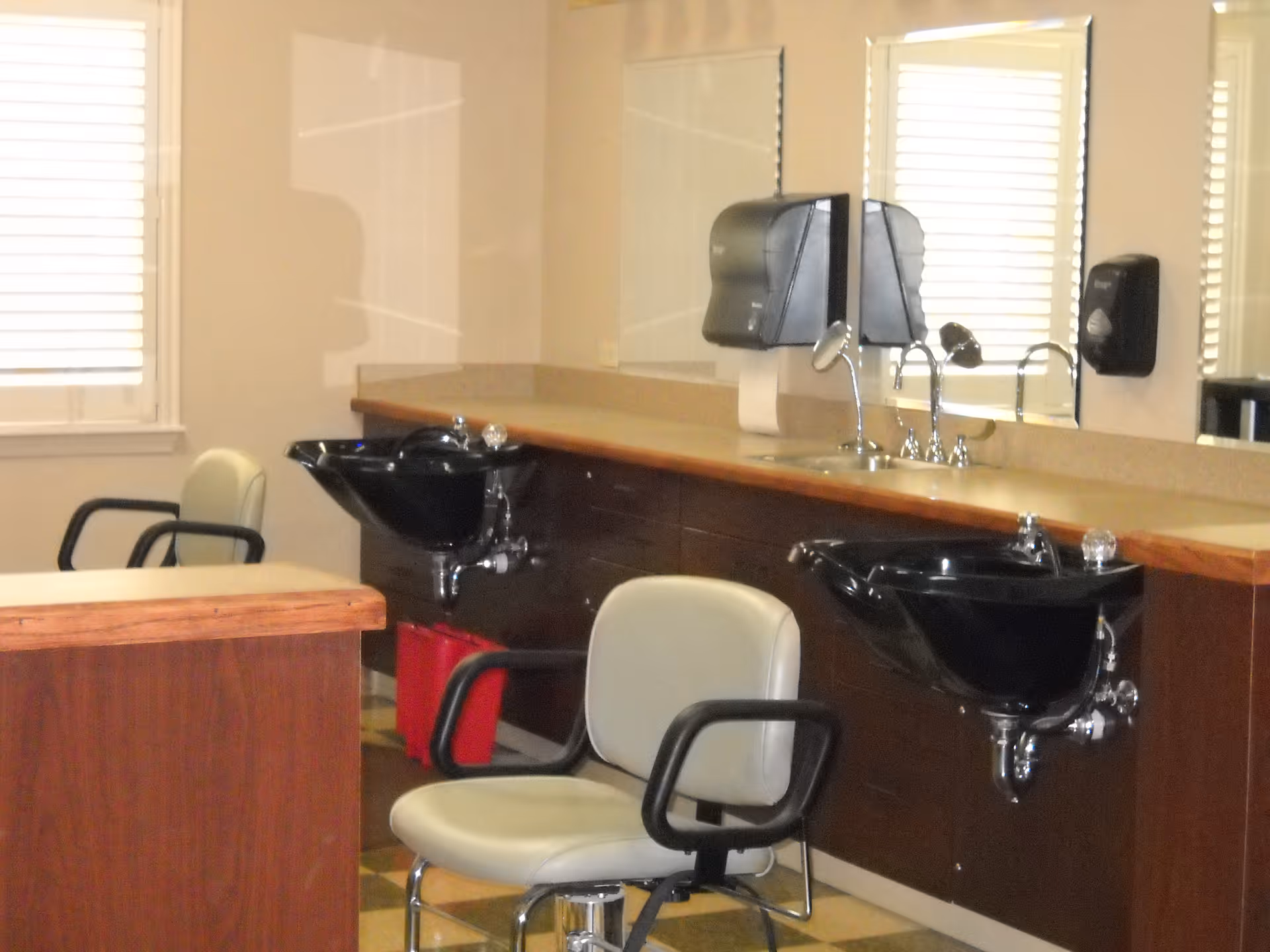 A salon-style interior with two black shampoo sinks and swivel styling chairs along a countertop and mirrors.