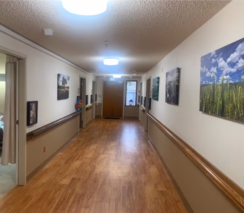 Long interior hallway with wood floors, handrails and framed artwork leading to a door at the end.