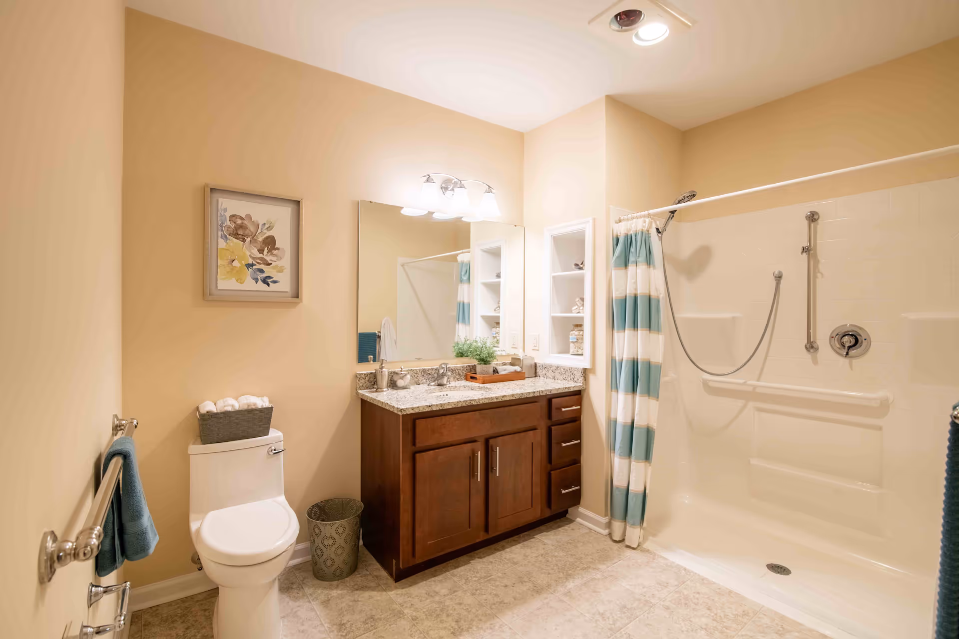 Well-lit bathroom featuring a toilet, wooden vanity with mirror, and a walk-in shower with a striped curtain and grab bars.