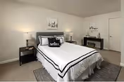 A neatly arranged bedroom with a bed dressed in white linens with black trim, nightstands and lamps, wall art, and a dresser.