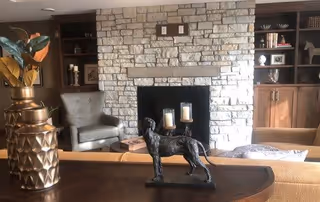 Cozy living room with a stone fireplace flanked by built-in shelves, seating, and decorative accents including a small dog statue on a table.