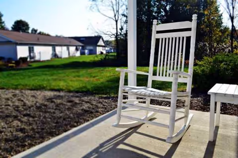 White rocking chair on a concrete patio with a small table and distant buildings.