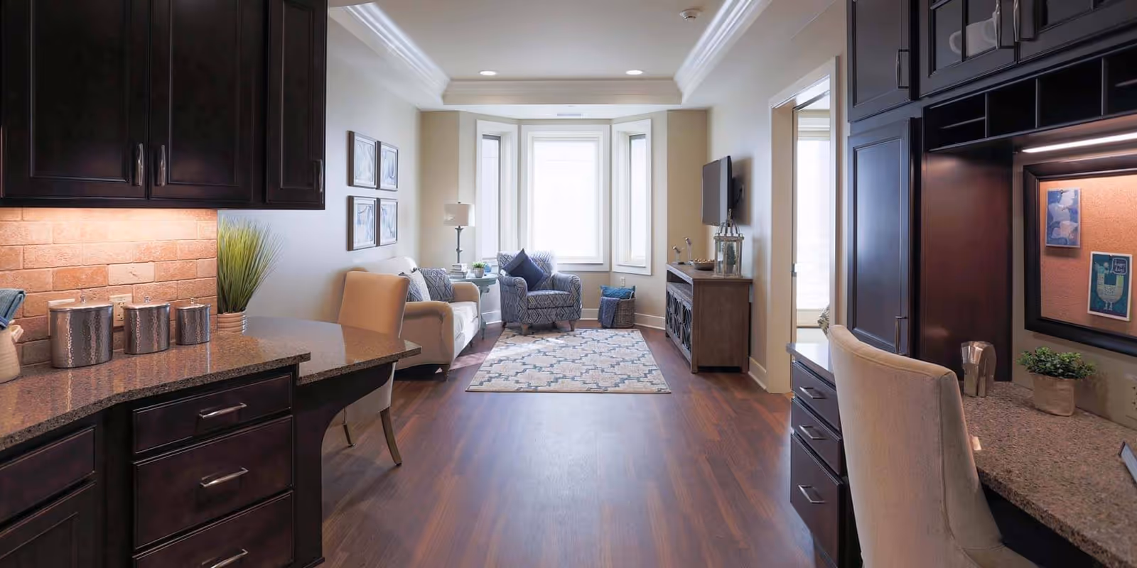 Open-plan living room and kitchen with dark cabinets, a countertop island in the foreground, sofa seating and a bay window in the background.
