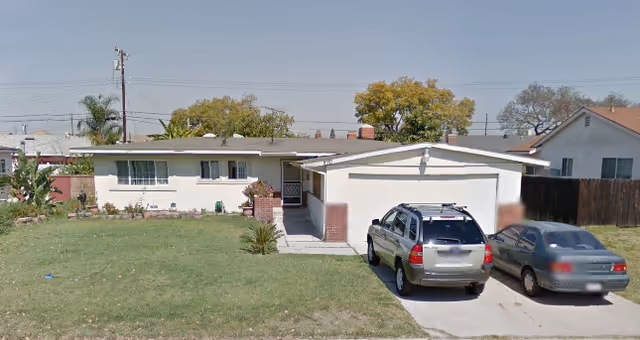 Single-story residential house with a front lawn and two cars parked in the driveway under a clear sky.