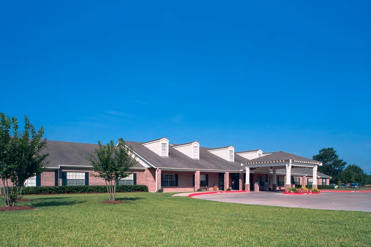Exterior view of a single-story brick building with a covered entrance, surrounded by green grass and small trees under a clear blue sky.