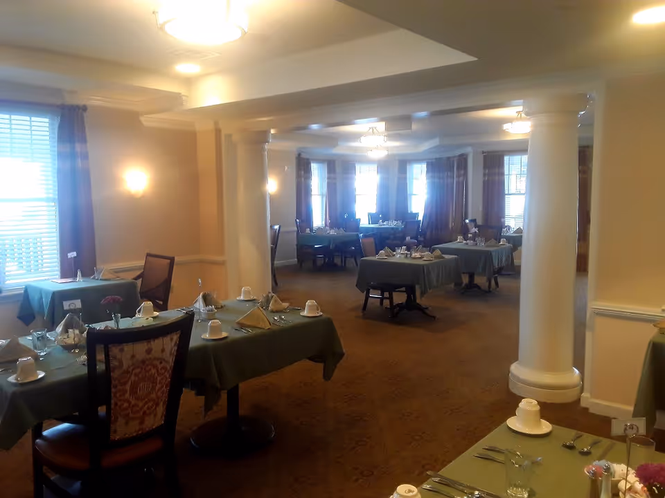 Spacious dining room with multiple tables set with cups and napkins, large columns, and warm lighting.